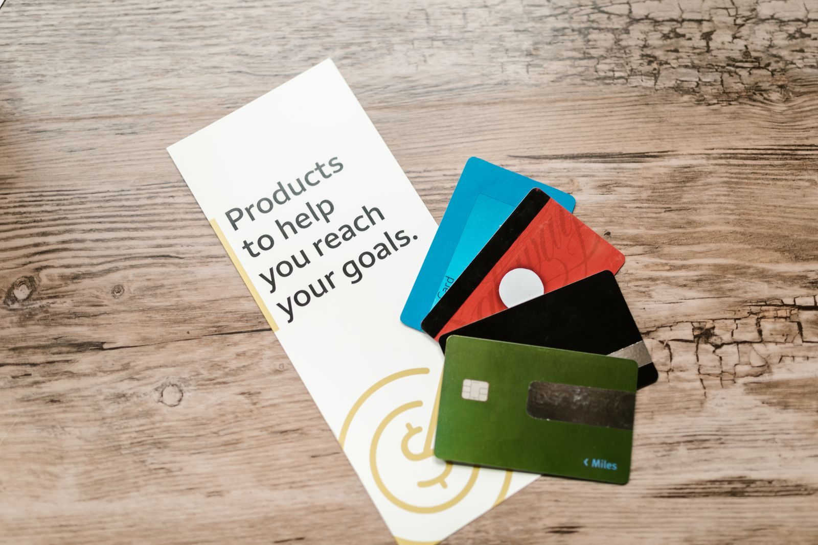 Several plain credit cards fanned on a wooden table beside a leaflet, a reminder of how people travel free with credit card points