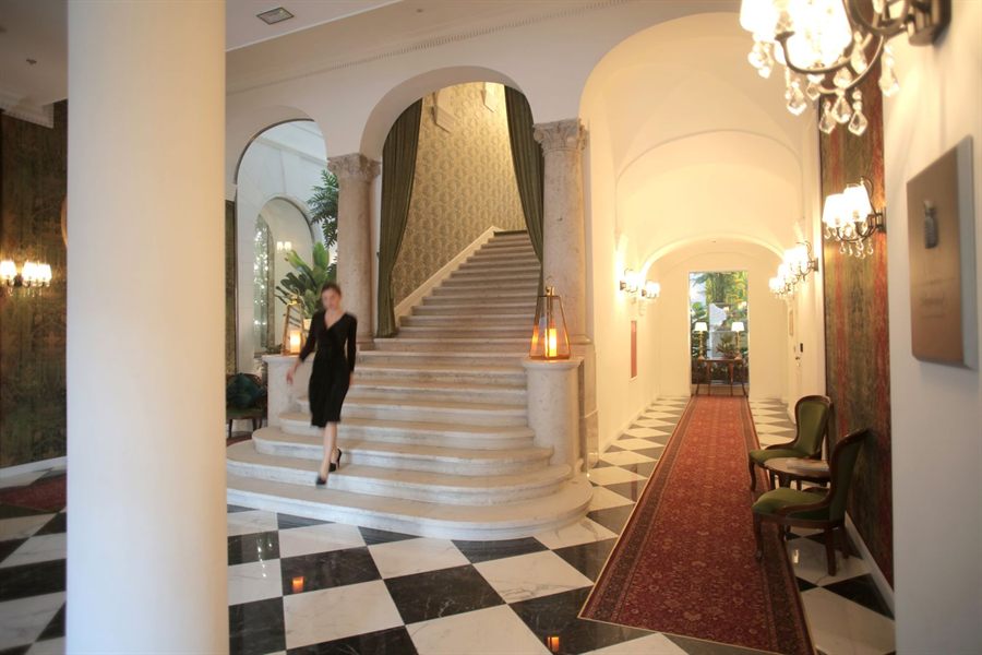 A guest walking down a sweeping staircase in an elegant hotel hall with a chandelier