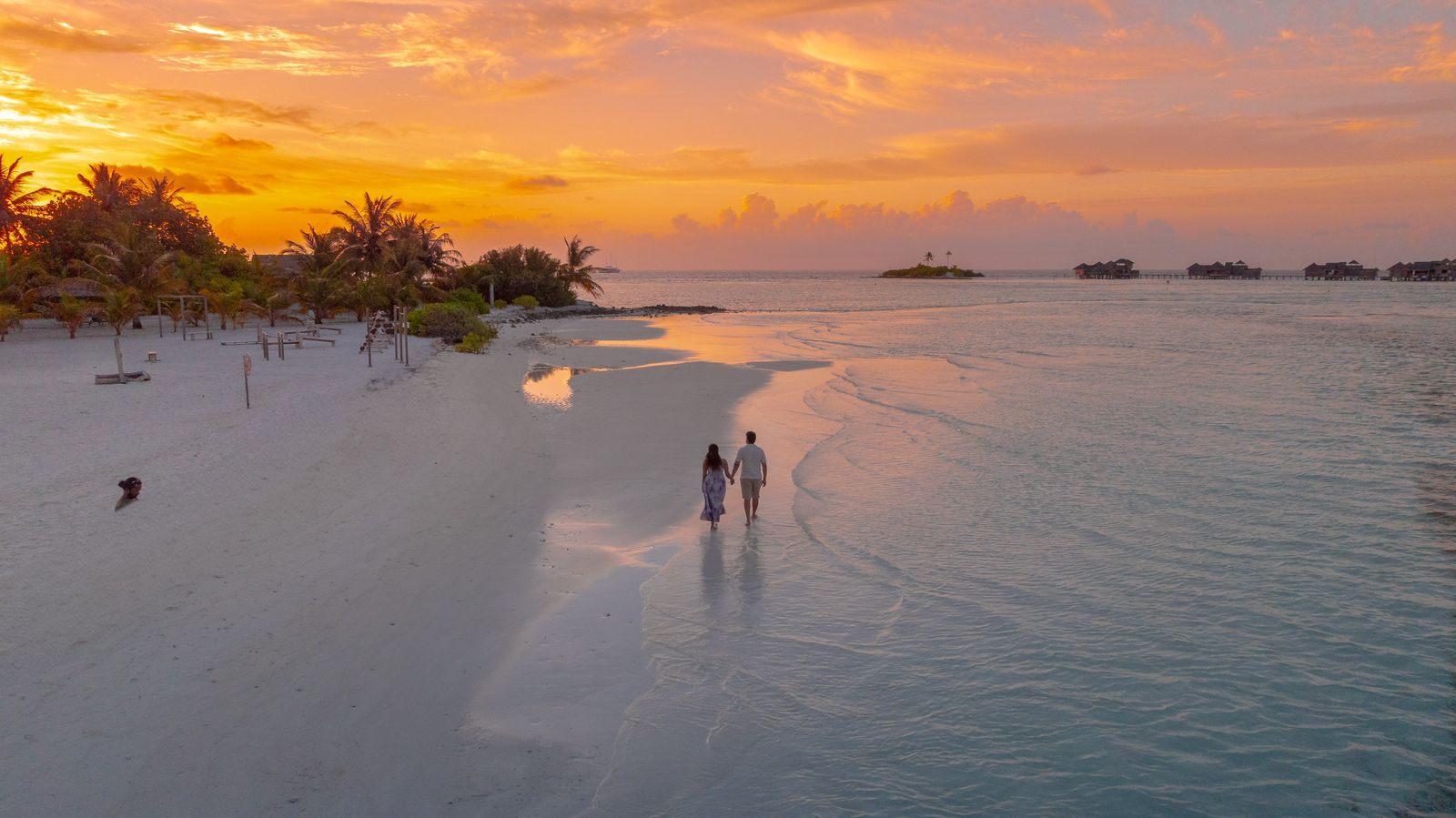 A couple walking along a white-sand island beach at sunset, the kind of trip people picture when they ask how to get free travel
