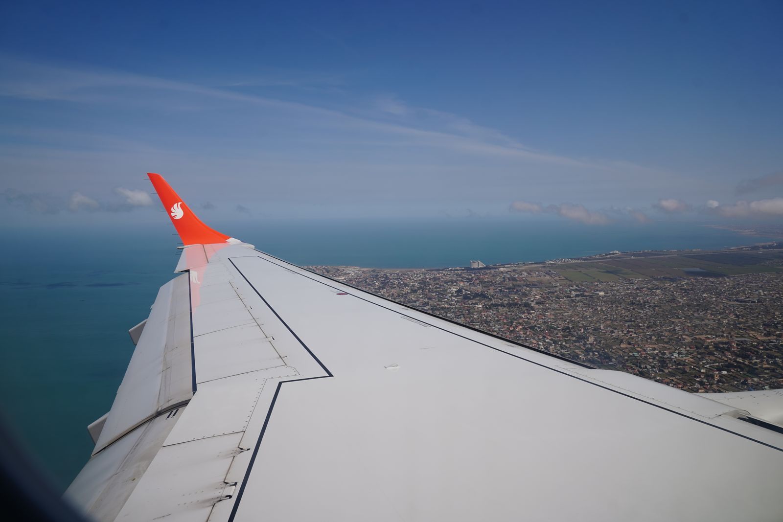 Airplane wing over a coastal city and blue sea, seen from a window seat