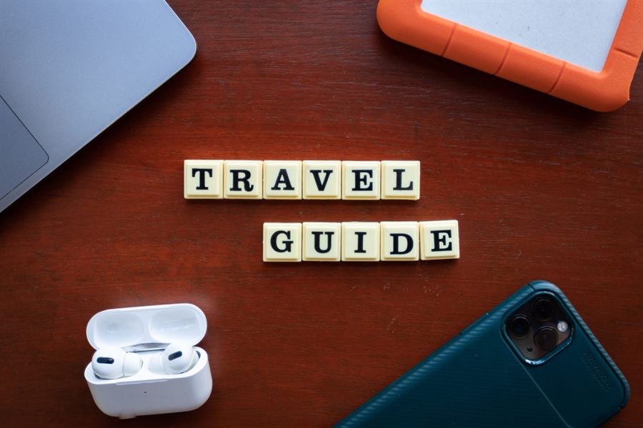 Letter tiles spelling TRAVEL GUIDE on a wooden desk with a phone and earbuds